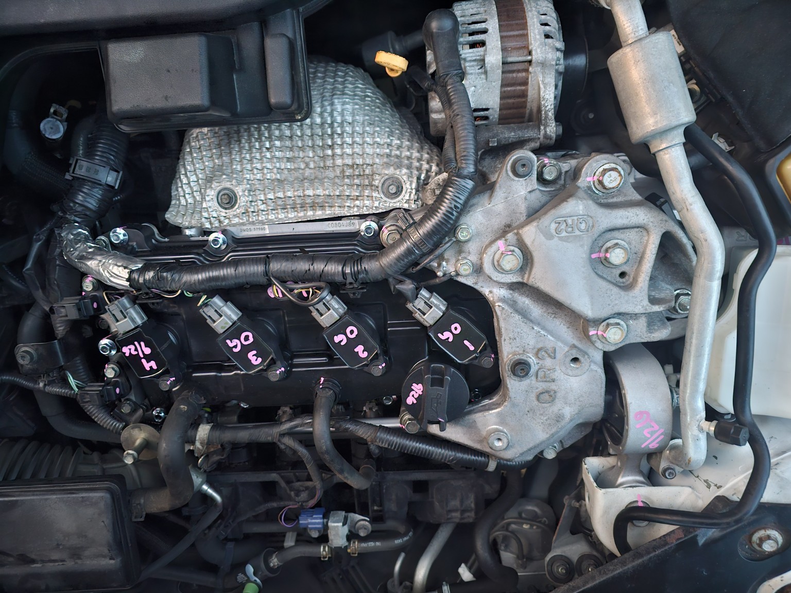 Engine bay showing valve cover, ignition coils, wiring, and marked fasteners